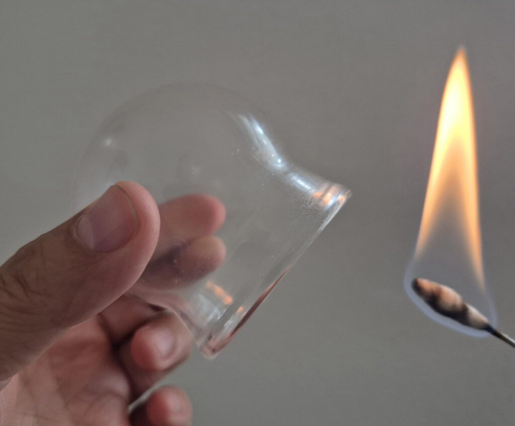 Abbildung eines Schröpfglases mit Flamme zum Herstellen des Unterdrucks.